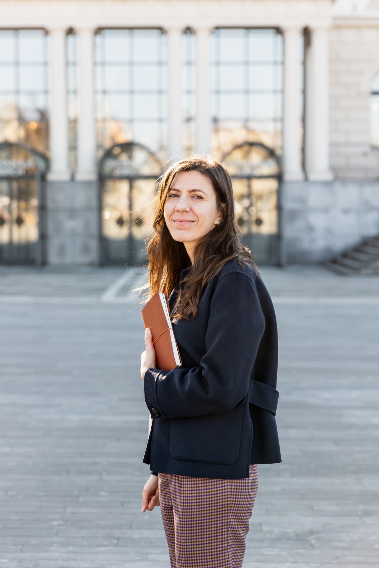 Andreea Stănescu holding her leather notebook outside a classical building